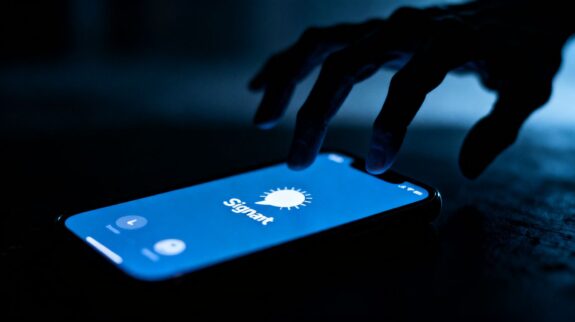 Signal app on phone with shadowy figure behind it.